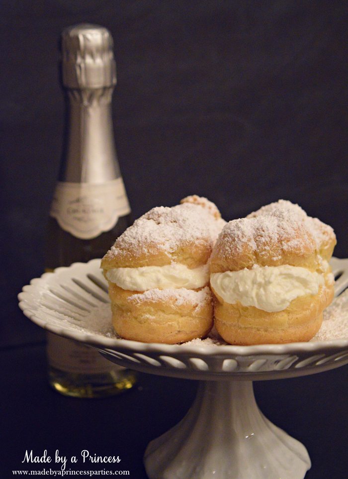 easy-champagne-cream-puffs-recipe-with-powdered-sugar-on-a-cake-stand-and-champange-on-the-side