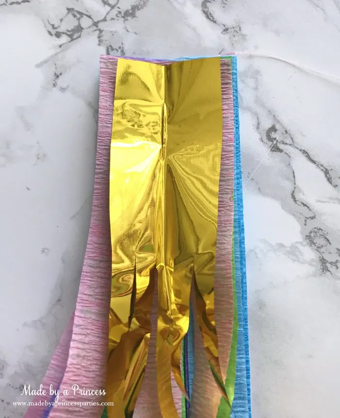 unicorn tail party idea tutorial place section of gold fringe curtain about the same width as crepe paper on stack of paper