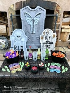 Teen Halloween Party Ideas simple table of snacks drinks and treats use tombstones as backdrop Made by a Princess #halloweenparty #teenhalloween